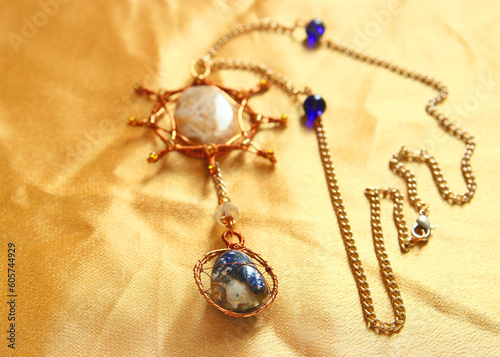 Sun and Earth pendant handmade from natural stones (agat, sodalite, carnelian) and copper wire on golden fabric.