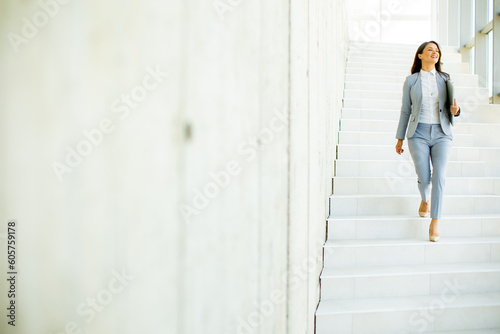 Young business woman walking down the stairs and holding laptop