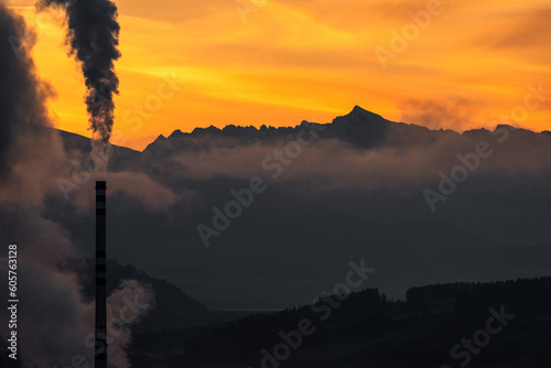 Smoking chimney and mountains with and colorful sky at background.