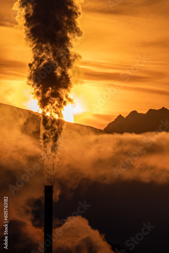 Smoke from chimny and colorful sky with sun and mountains at background