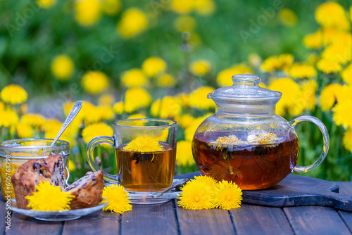 Healthy dandelion flower tea in a glass teapot on the wooden table along with sweet jam and cherry muffin in the spring garden, closeup