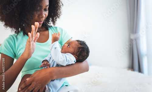 half Nigeria half Thai, 1-month-old baby newborn son, looking at mother while his mother being held and sitting on a white bed, to relationship in family and infant newborn concept.