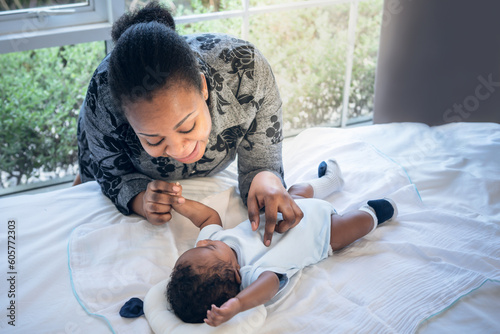 African mother smile and talking with a 2-month-old baby newborn son who is lying on white bedt, to relationship in African family and baby newborn concept. photo