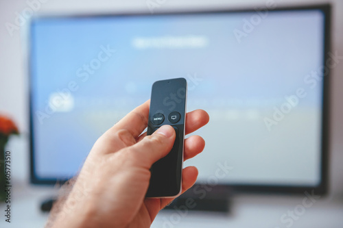 An unrecognizable adult is persistently making decisions and changing channels while holding a remote control in front of a television set indoors.