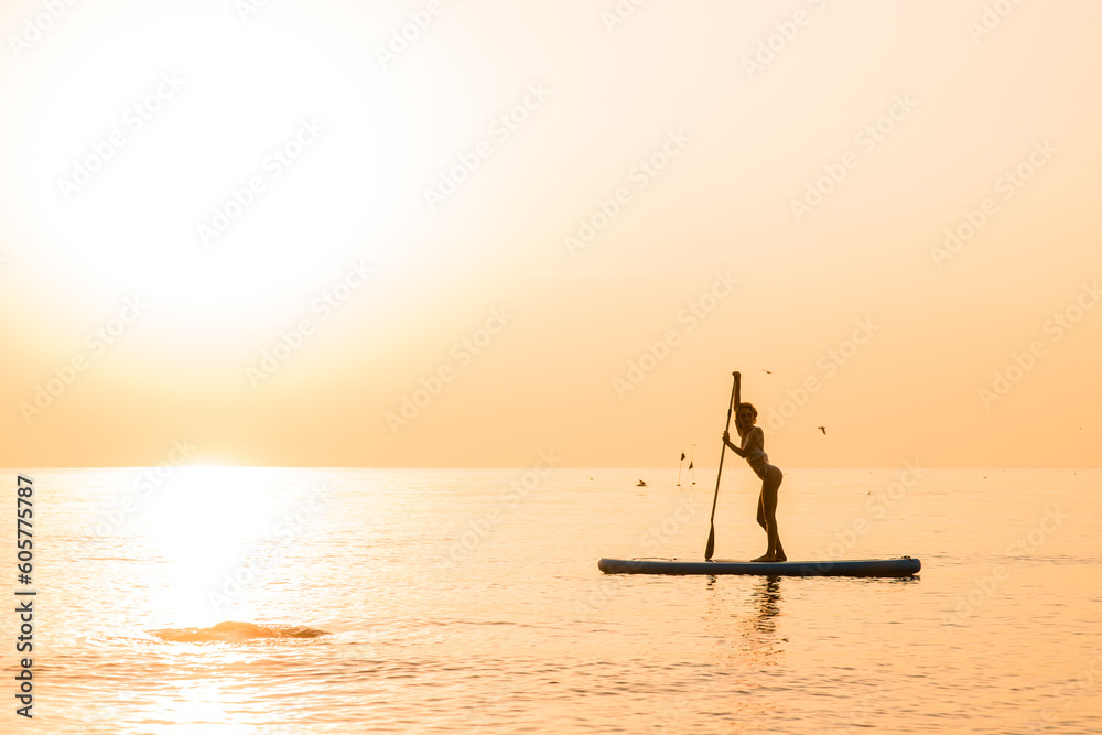 Stunning silhouette of beautiful girl floating on on the surf board