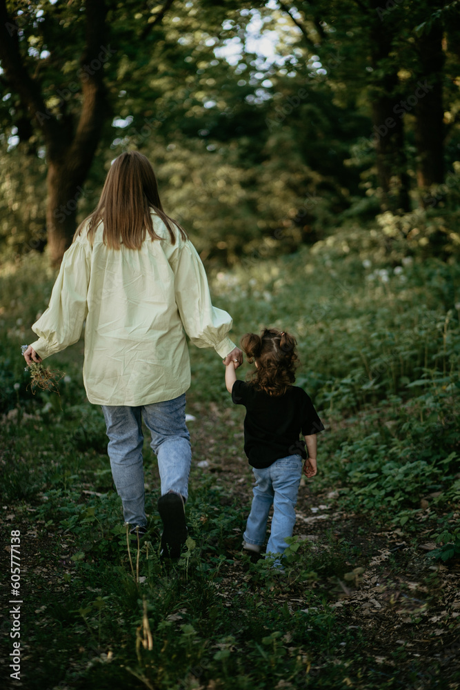 Fototapeta premium Mother holds children's hands and walks through the forest