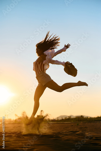 Playful woman has fun while jumping at sunset in summer day.