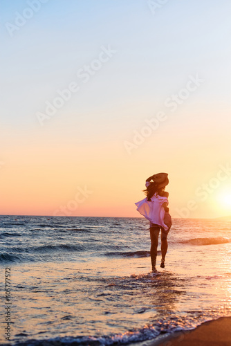 Rear view of woman has fun at summer sunset while running through water on beach.