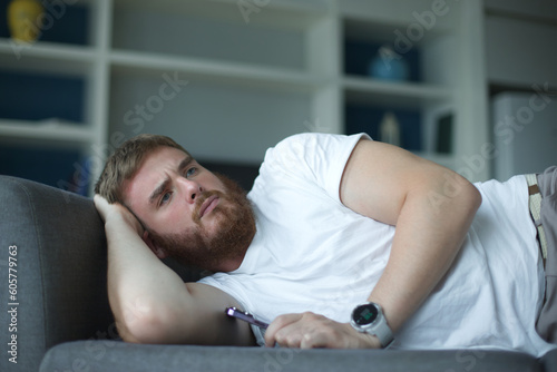 Young bearded anxious worried man sleep at home on couch with his cell mobile phone in living room. Smartphone addiction concept. 