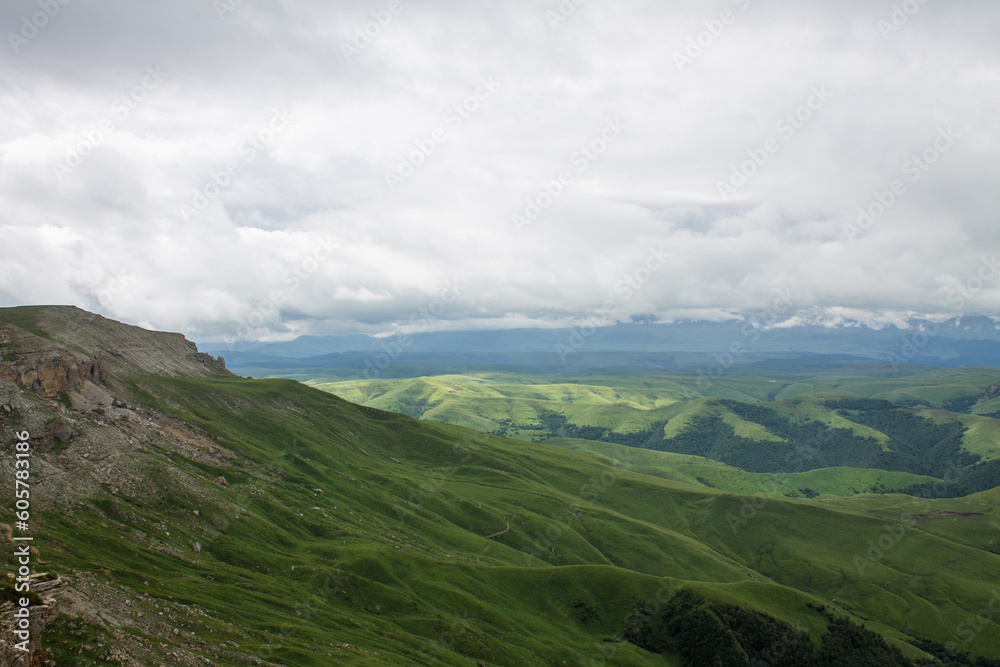 Dramatic landscape - a beautiful view from the Bermamyt plateau in Karachay-Cherkessia - green hills in the morning haze and cloudy sky