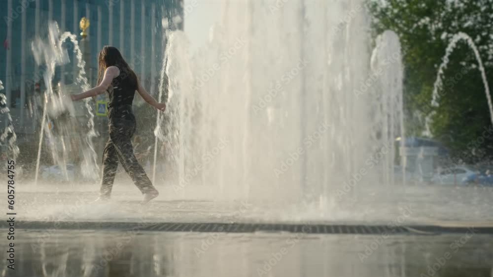 Teenage girl running in the city fountain under splashes of water on a ...