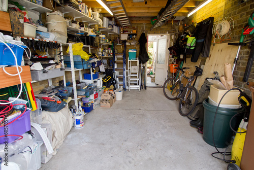 Interior of typical UK garage full of shelves, tools, bikes, paint and ladders.