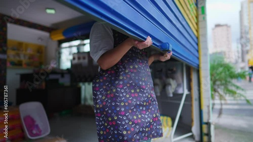 Female Business Owner of Local Store opening garage storefront. Young entrepreneur woman wearing apron starting the day routine