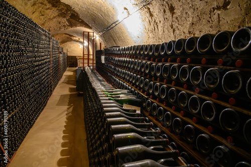 Walking in deep undergrounds caves with bottles on wooden racks, making champagne sparkling wine from chardonnay and pinor noir grapes in Epernay, Champagne, France photo
