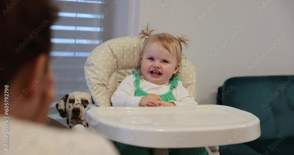 One year old beautifull baby girl with blonde hair and blue eyes sitting in child chair laughing and playing peek a boo with mother. High quality 8k shot. Having a good time. Eating. Educating. Fun. One year old beautifull baby girl with blonde hair and blue eyes sitting in child chair laughing and playing peek a boo with mother. High quality 8k shot. Having a good time. Eating. Educating. Fun.