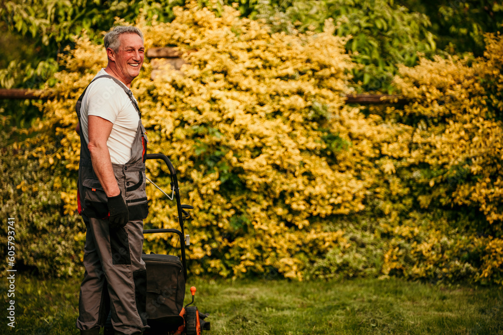 The male worker mows the grass on the site, cares for the garden, uses a gasoline lawn mower The male worker mows the grass on the site, cares for the garden, uses a gasoline lawn mower