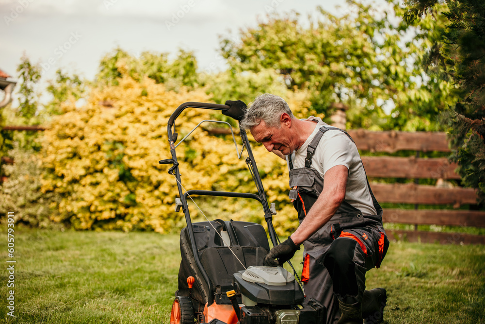 Man checking and repairing a lawn mower in his backyard.