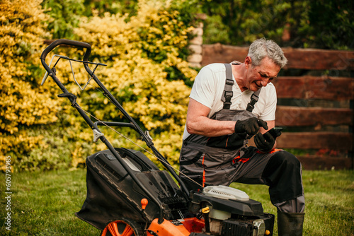 A senior man using his phone and calling a service guy to fix his broken lawnmower. photo