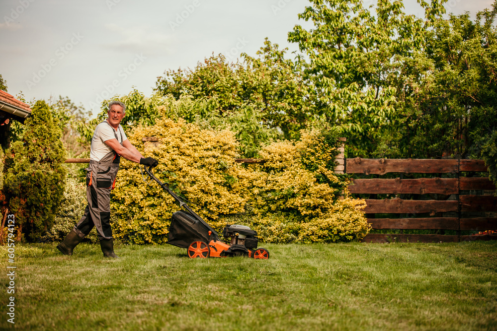 A mature man is pushing a lawnmower around a lawn. Copy space A mature man is pushing a lawnmower around a lawn. Copy space
