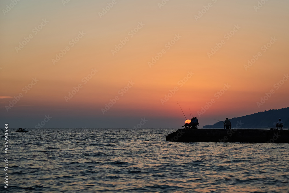 Sea pier at sunset, where fishermen are fishing