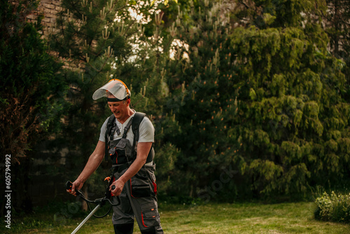 Senior caucasian man farmer gardener standing in the field with a string trimmer
