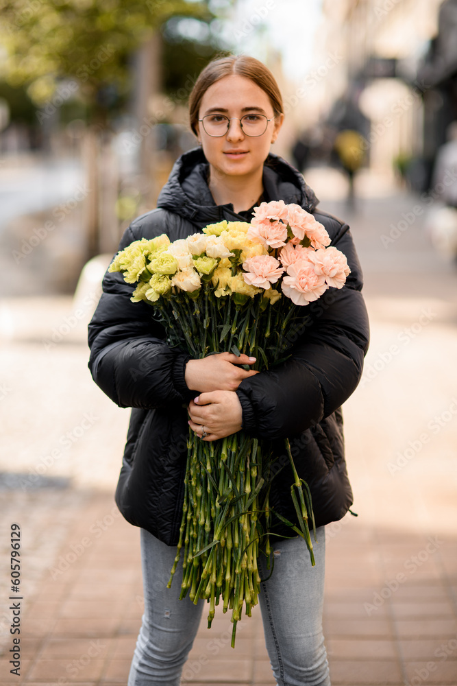 Fototapeta premium Young beautiful woman with large bouquet of yellow, pink, lemon and milk colors carnations in hands.