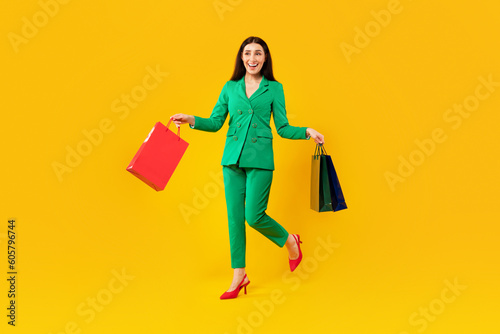 Full length shot of excited woman walking with bright shopping bags, enjoying successful seasonal sales