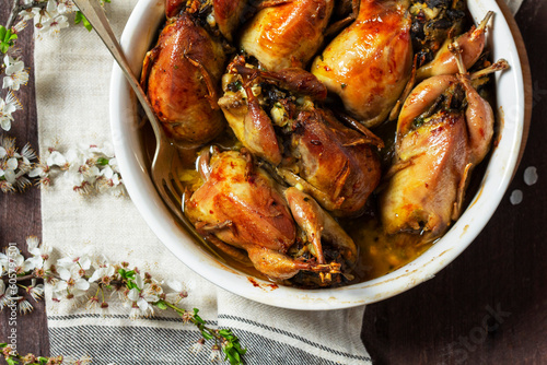 Baked quail stuffed with mushrooms, eggs and bread in a ceramic form on a wooden table.