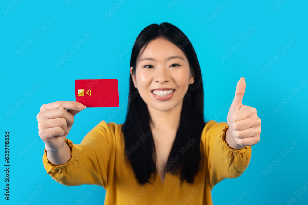 Cheerful chinese young woman showing bank card on blue Cheerful chinese young woman showing bank card on blue