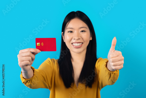 Cheerful chinese young woman showing bank card on blue © Prostock-studio