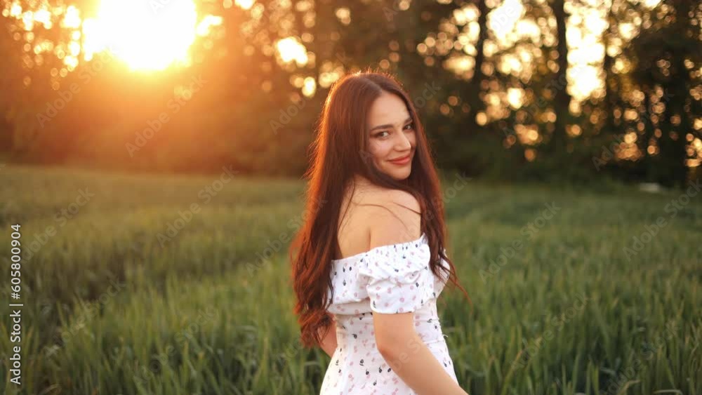 A young girl in a summer dress walks in slow motion through a green field of wheat. Beautiful carefree woman enjoying nature and sunlight in wheat field at sunset A young girl in a summer dress walks in slow motion through a green field of wheat. Beautiful carefree woman enjoying nature and sunlight in wheat field at sunset