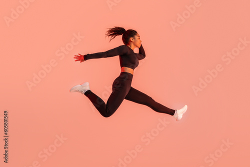 Fototapeta Naklejka Na Ścianę i Meble -  Athlete black woman in sportswear jumping and having workout on red neon studio background, copy space, full length