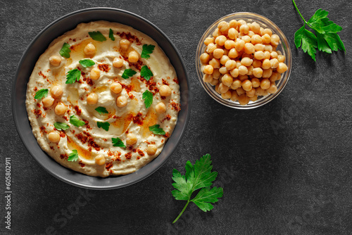 Hummus with olive oil, red pepper and parsley in grey bowl, on slate stone plate round, dark background, top view