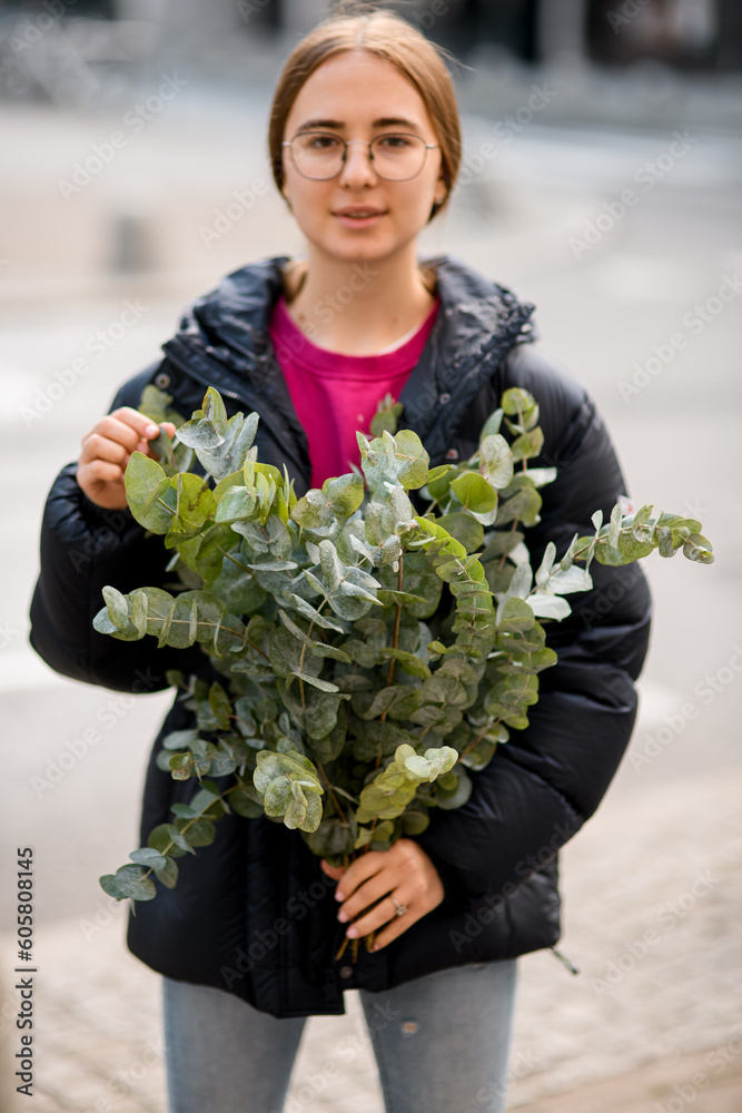 Fototapeta premium Young woman holding bouquet with eucalyptus branches in hands on blurred background