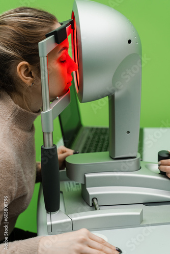 Corneal topography eye vision test for visual description of the shape and power of the cornea. Red light of the corneal topographer shines on the woman at topography examination. photo