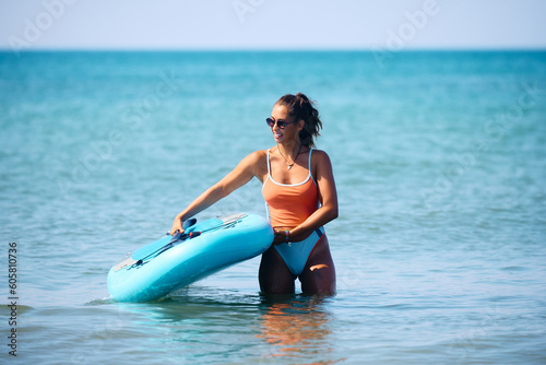 Happy female surfer SUP boarding in summer day at sea.