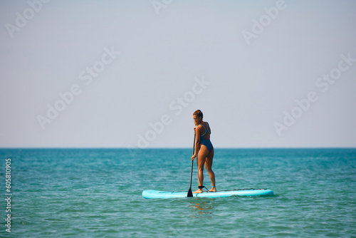 Happy female surfer enjoys in standup paddleboarding at sea.