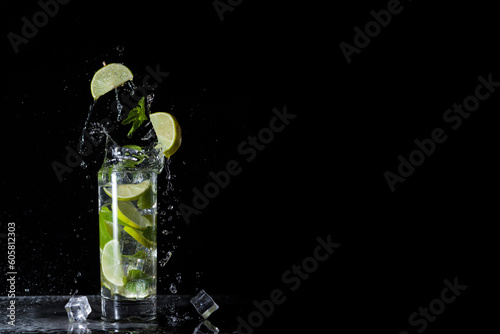 Cold mojito cocktail with mint lime and ice on a black background with splashes and falling ice