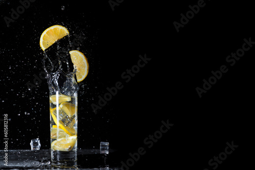 Cool and fresh drink of orange lemonade with orange slices and ice on a black background with falling orange slices and ice