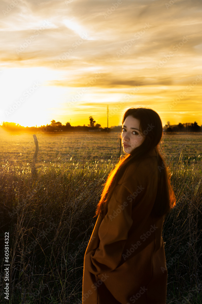 Fototapeta premium Beautiful woman drinking coffee in a field with sunset in the background