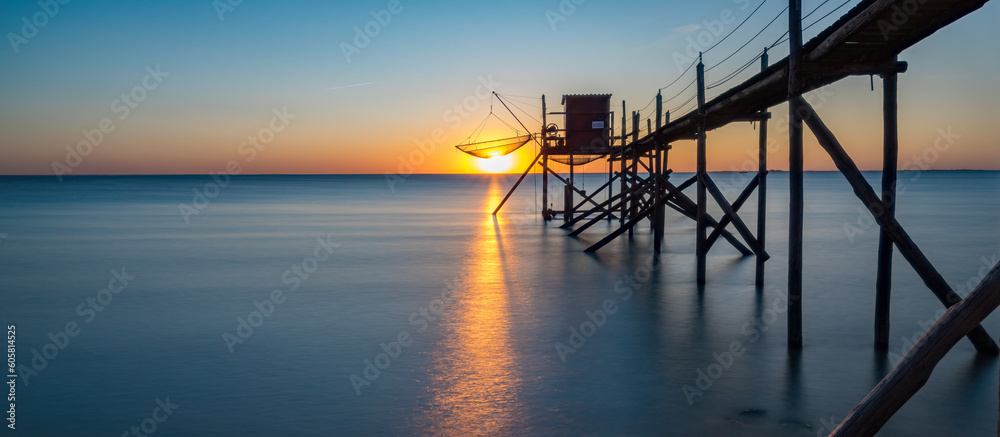 A fishing hut called carrelet with craft lifting net at sunset. Esnandes, charente maritime, France. The sun is caught in the net.