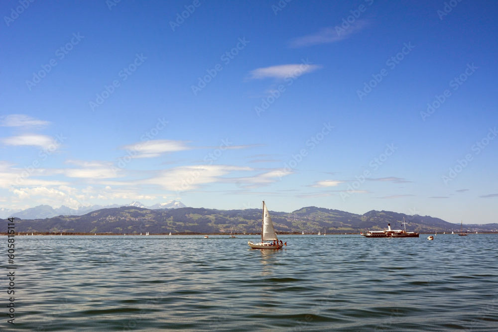 Yachts and a small ship sail across the sea against the background of distant mountains and a blue sky