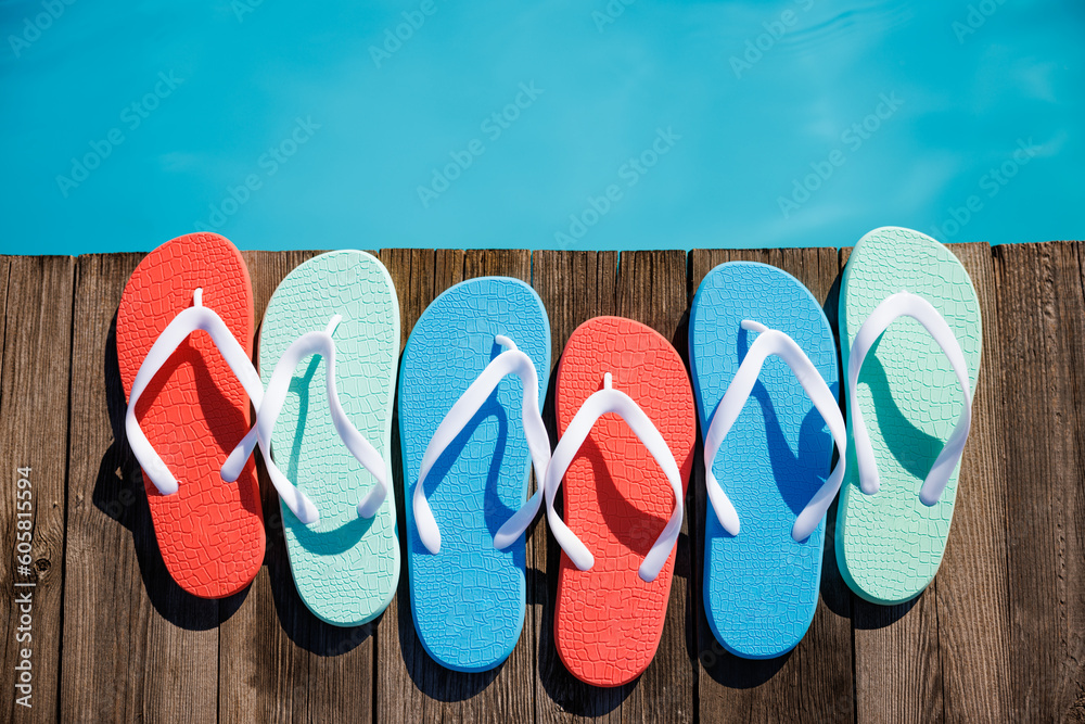 Naklejka premium Beach flip-flops on wooden planks near swimming pool