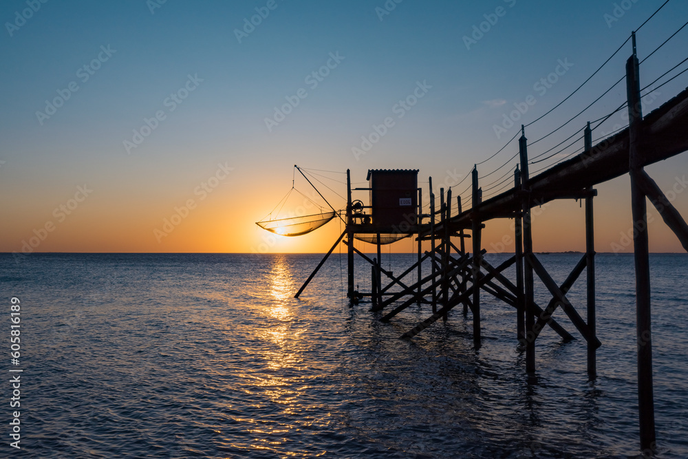 A fishing hut called carrelet with craft lifting net at sunset. Esnandes, charente maritime, France. The sun is caught in the net.