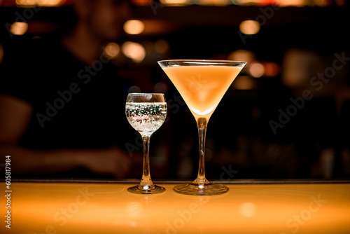 Glass of fresh yellow martini cocktail and glass with transparent bubble liquid nearby