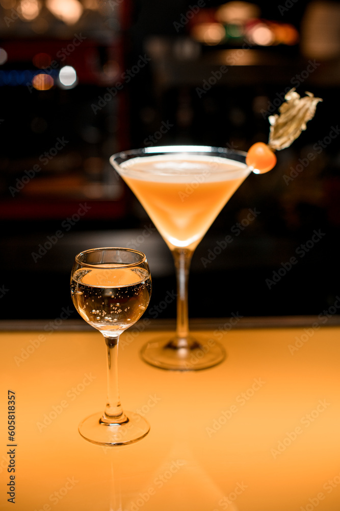 Bar counter with two alcoholic drinks: glass with champagne and fresh martini cocktail decorated with physalis Bar counter with two alcoholic drinks: glass with champagne and fresh martini cocktail decorated with physalis