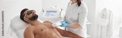 Cosmetologist does laser epilation of chest to athletic man using modern equipment in clinic photo