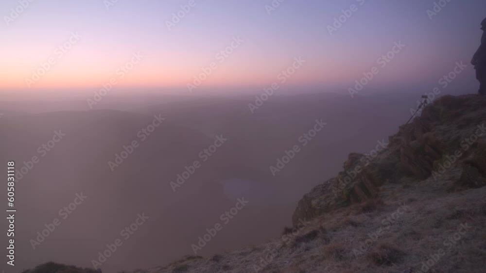 A photographer checking his camera on top of a mountain in crazy foggy sunrise weather conditions A photographer checking his camera on top of a mountain in crazy foggy sunrise weather conditions