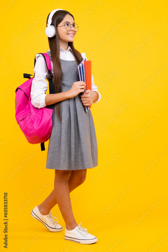 Back to school. Schoolgirl student in headphones with school bag backpack hold book on isolated studio background. School and education concept. Happy face, positive and smiling emotions Back to school. Schoolgirl student in headphones with school bag backpack hold book on isolated studio background. School and education concept. Happy face, positive and smiling emotions