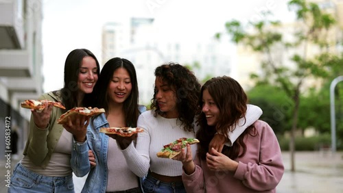 Four young girls having fun while eating pizza on street.